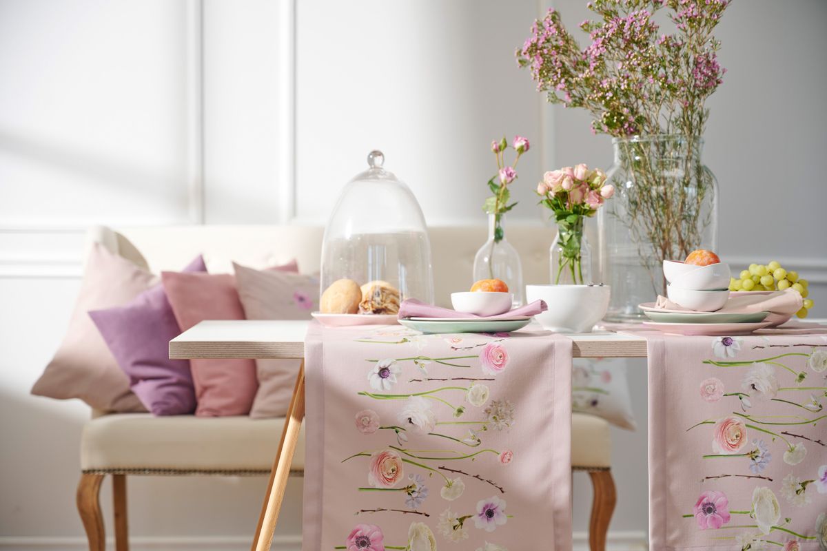 Tisch mit Tischlaufer rosa mit Tulpenmotiv, darauf Teller, Schuesseln, Eierbecher, Vasen