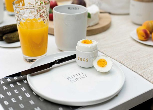 weißer Teller, Tasse und Eierbecher aus weißem Porzellan mit Aufschrift und schwarz-weiße Mottoserviette 