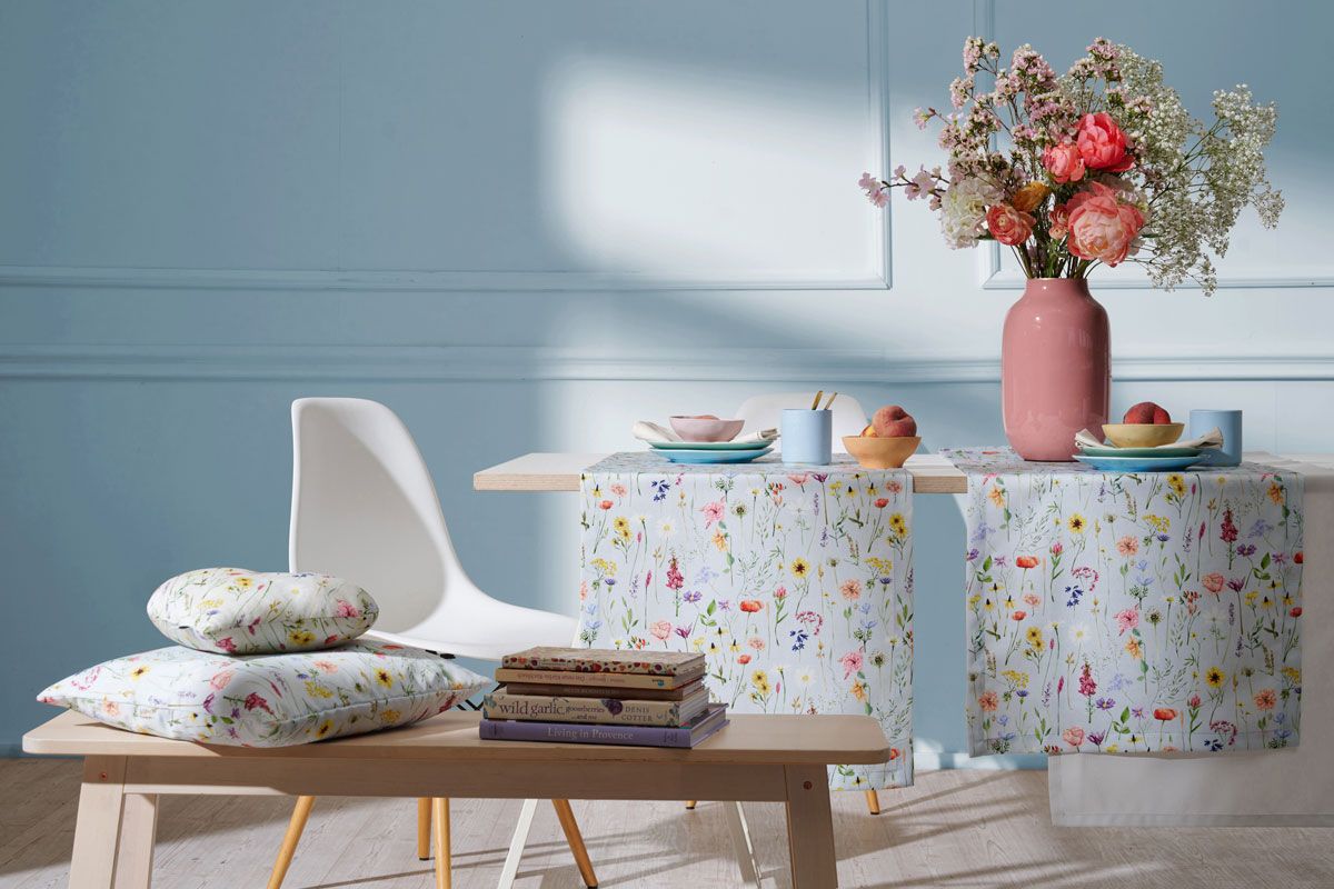 Tischdecken und Kissen mit Blumenmotiv auf Tisch und Bank